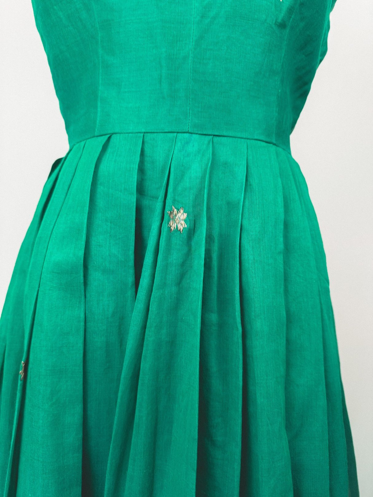 Green 1950s women’s dress featuring pleats and a starburst embellishment on the bodice.