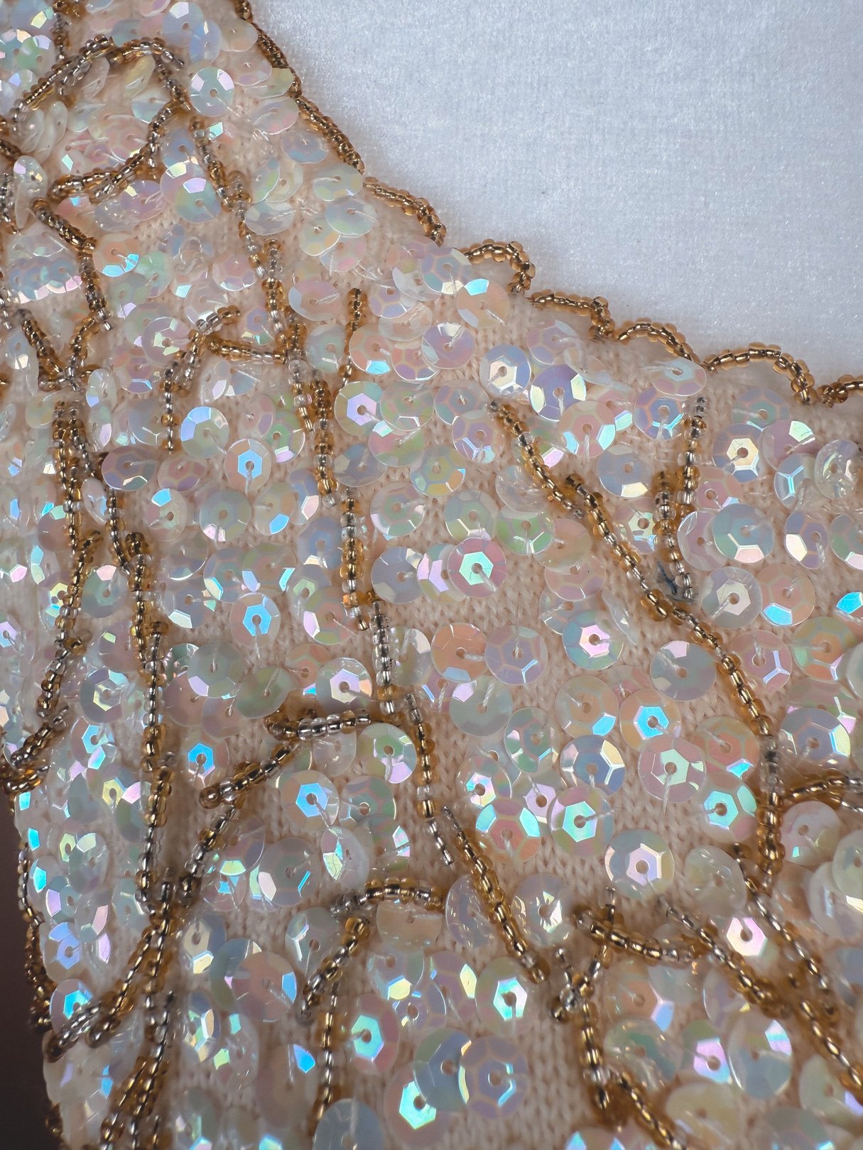 A white 1960s women's top adorned with iridescent sequins and gold beading.