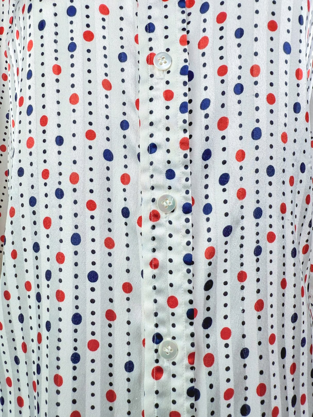 Blouse featuring a white background with red and navy polka dots, showcasing button details, typical of 1980s women's fashion.