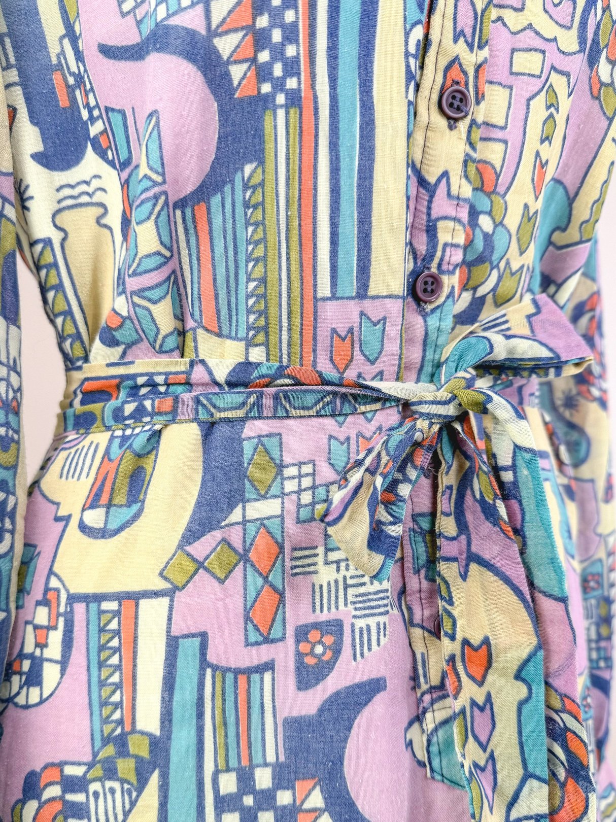 Cream 1970s Metropolis Dress featuring a colorful abstract pattern, long sleeves, and a tied waist detail.