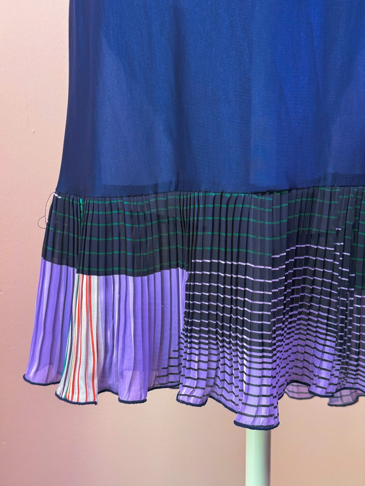 Flowy green pleated skirt with a multicolored, striped hem, inspired by 1970s fashion for women.