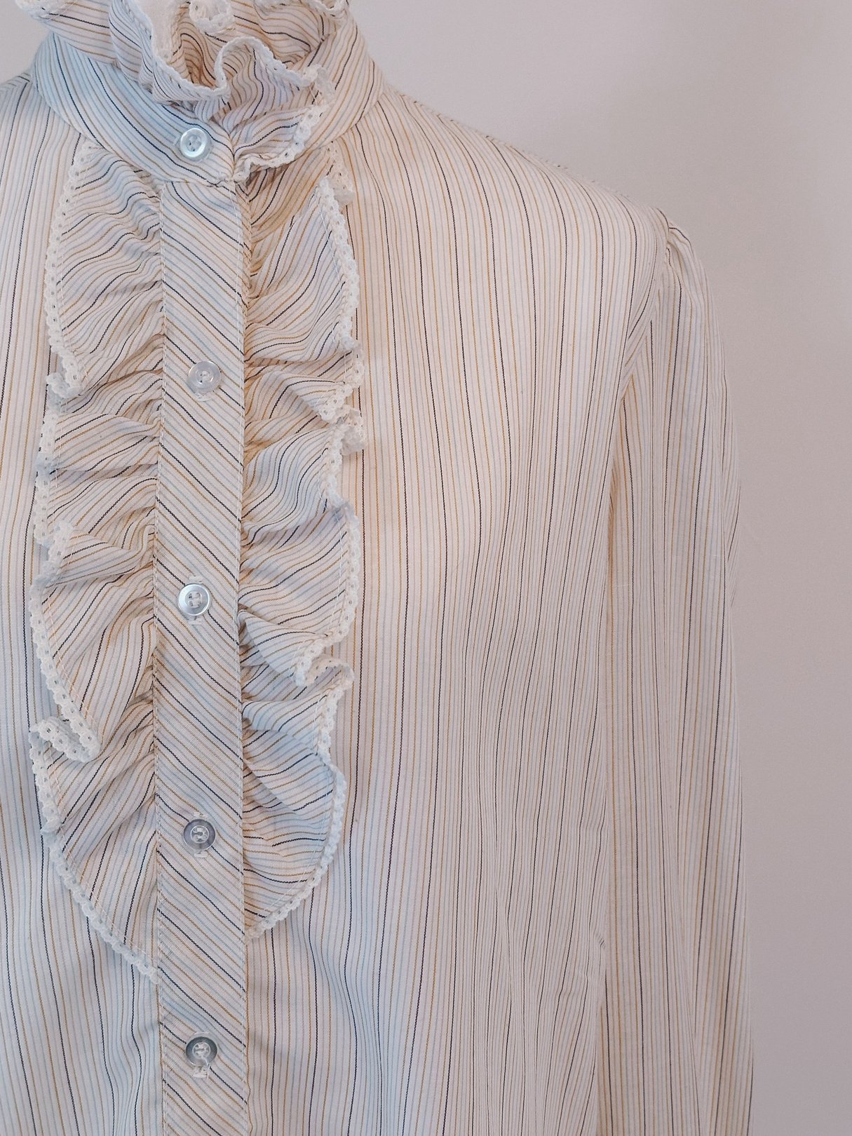 Cream blouse with a ruffled neck and intricate pink, orange, and blue stripes, resembling a 1970s style.