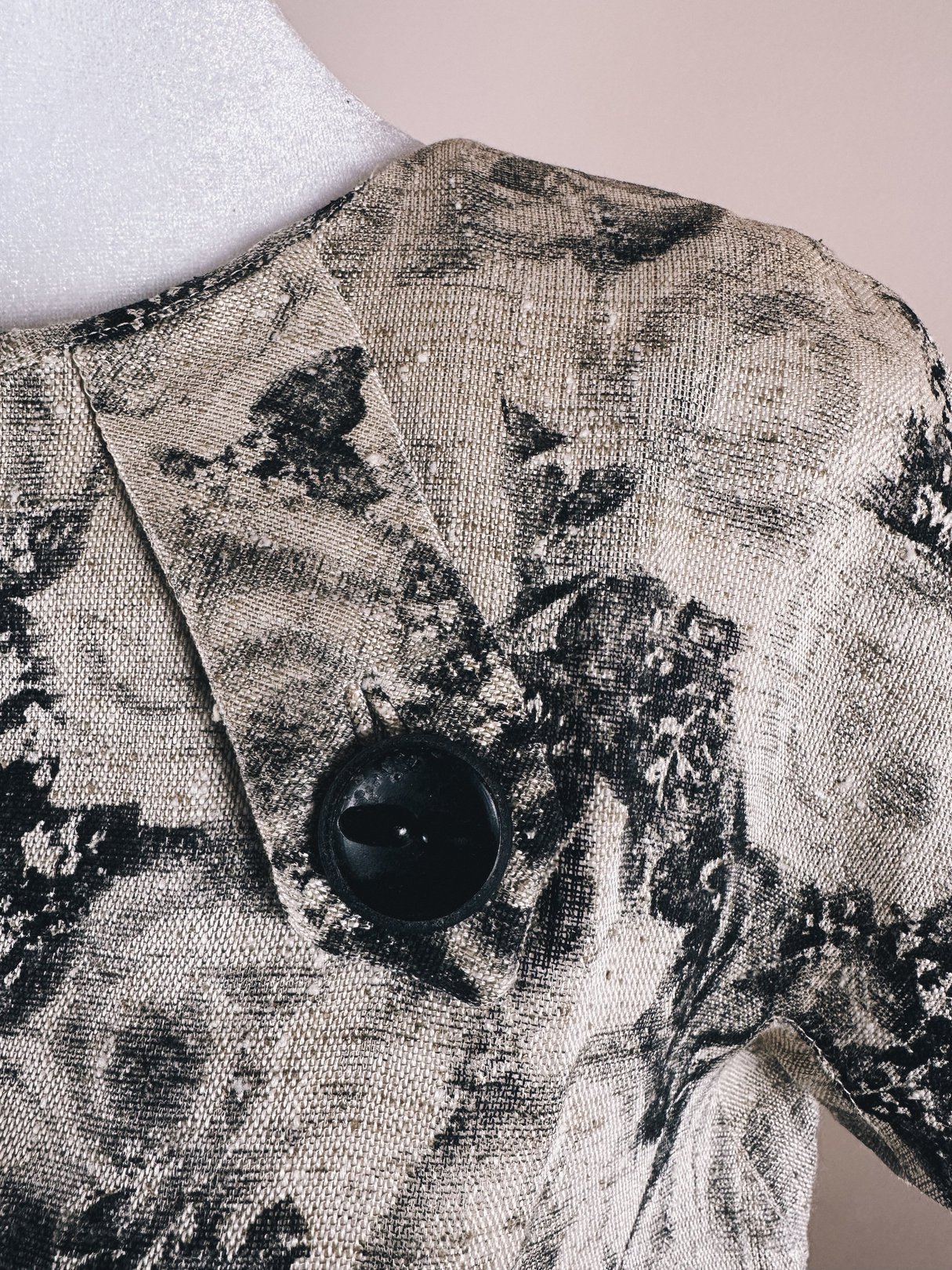 The dress features a textured fabric with a black and cream rose pattern and a large black button on the shoulder.