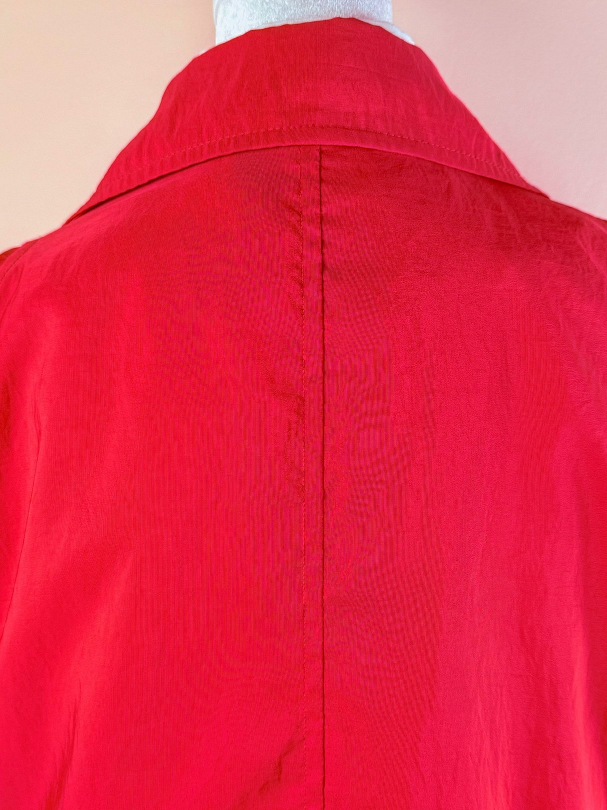 Red women's rain jacket from the 1980s featuring a classic collar and a smooth, lightweight fabric.