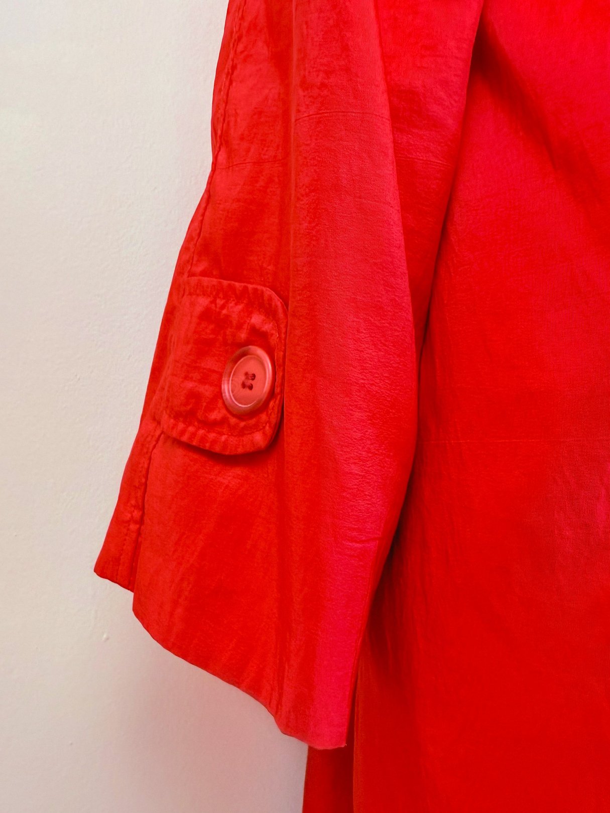 Red women's rain jacket featuring a 1980s design with a button detail on the sleeve.