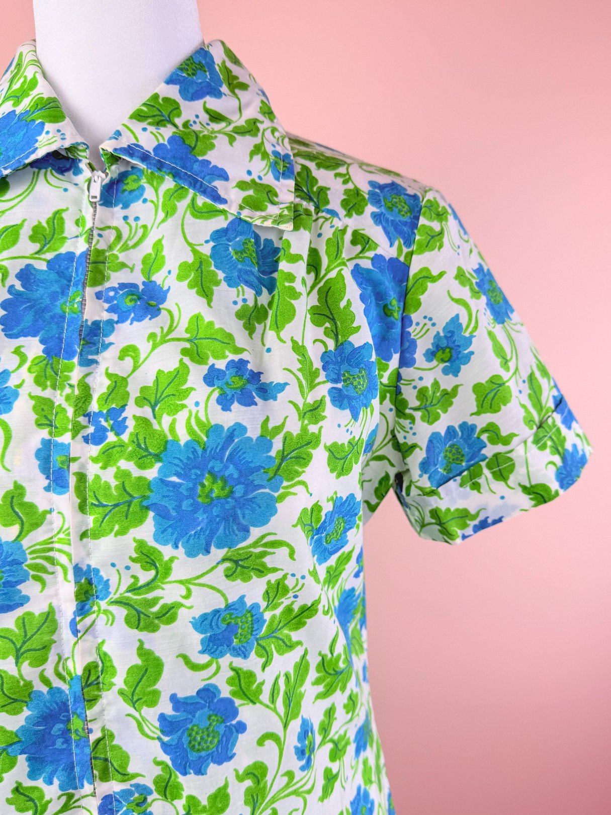 Button-up dress featuring a white fabric with a blue and green floral pattern, styled for women and inspired by the 1960s.