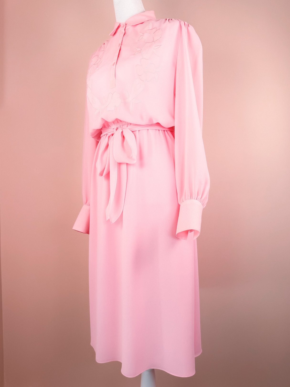 Flowy bubble gum pink women's dress from the 1980s with long sleeves, a tied belt, and floral embroidery.