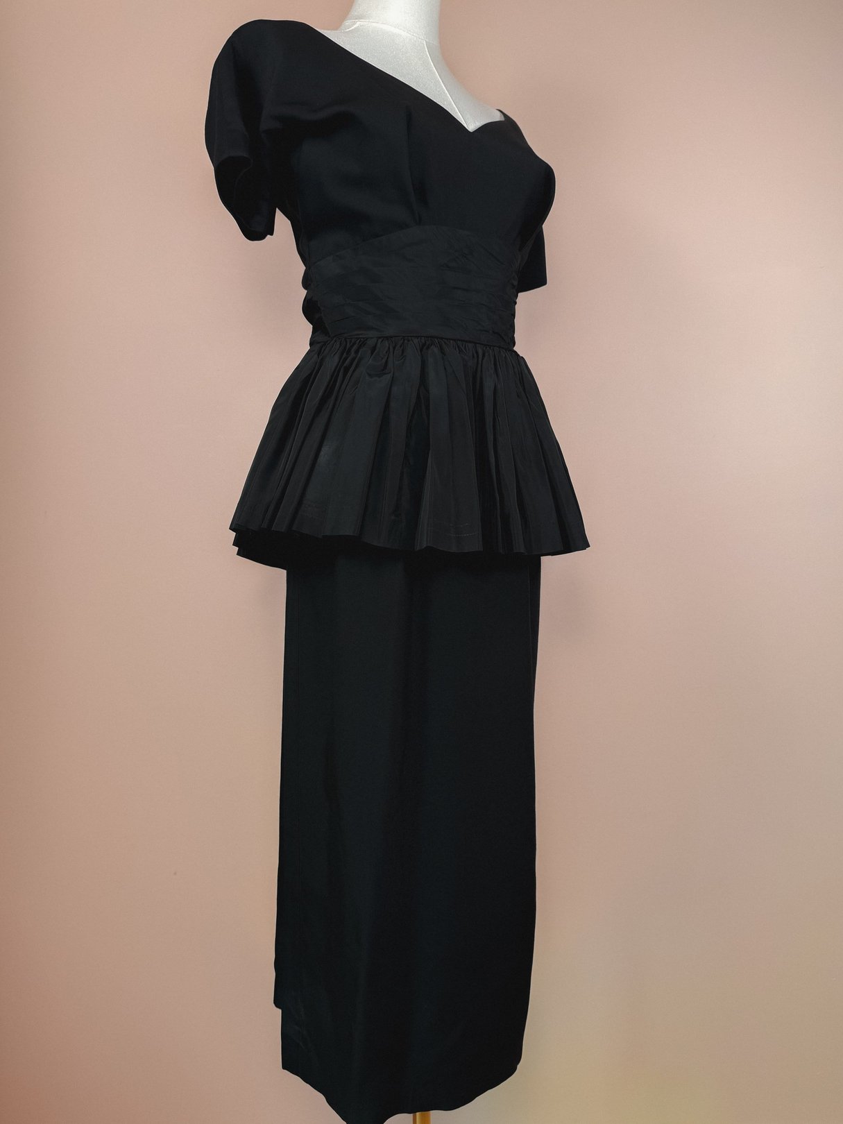 A 1950s black women's dress featuring a fitted top with puff sleeves and a pleated peplum at the waist.