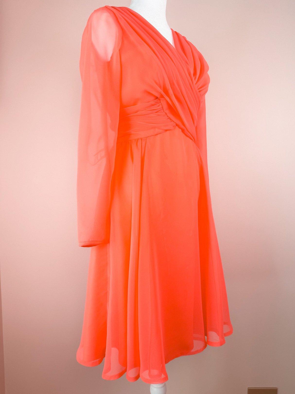 Coral Soirée Dress featuring long sleeves, a fitted bodice with a twisted design, and a flared skirt, representative of 1960s women's fashion.