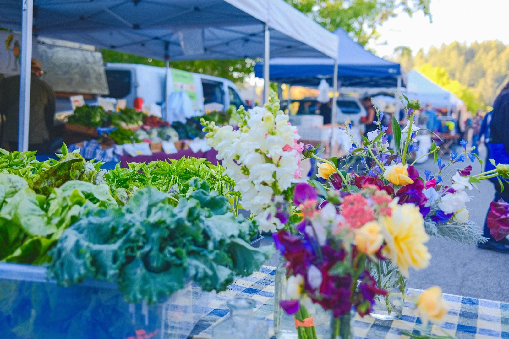 A vibrant farmers market display featuring fresh greens and colorful flower bouquets under blue tents.