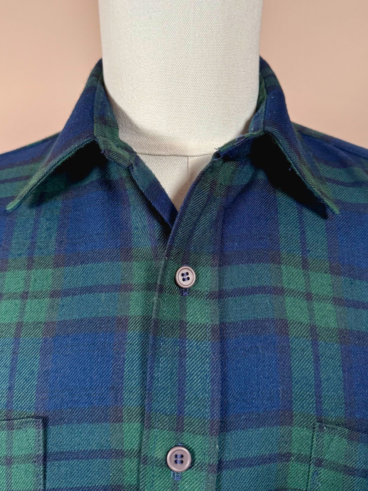 Navy blue and green plaid shirt for men, featuring a classic collar and button closure, representative of 1950s fashion.