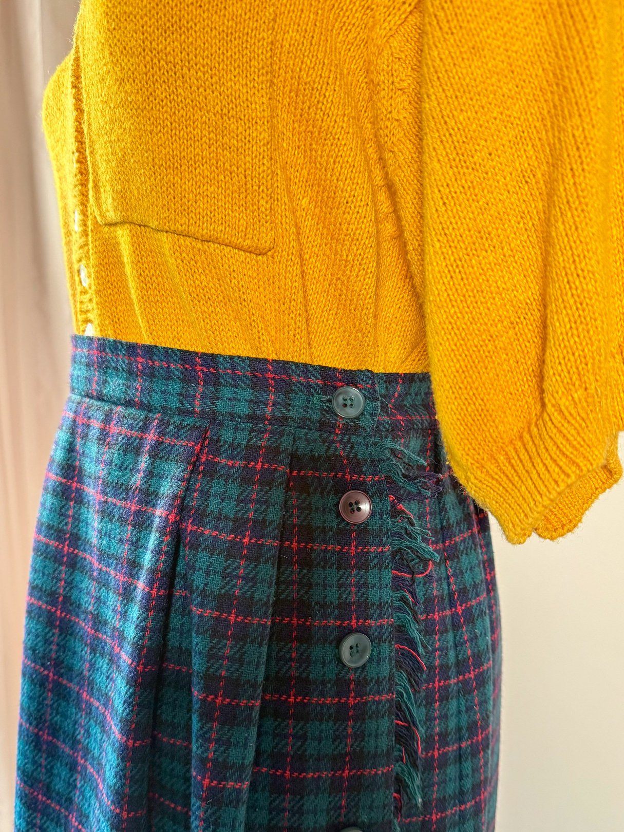 Green plaid skirt with a 1970s style and side button detailing, paired with a yellow knit top.