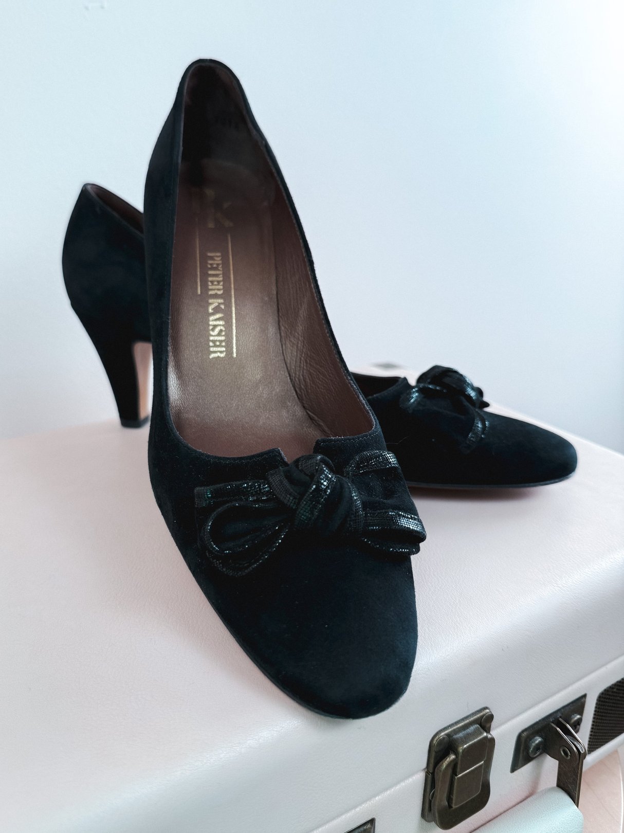 Black suede pumps featuring a bow detail on the toe and a mid-height heel, reflecting a 1970s style for women.