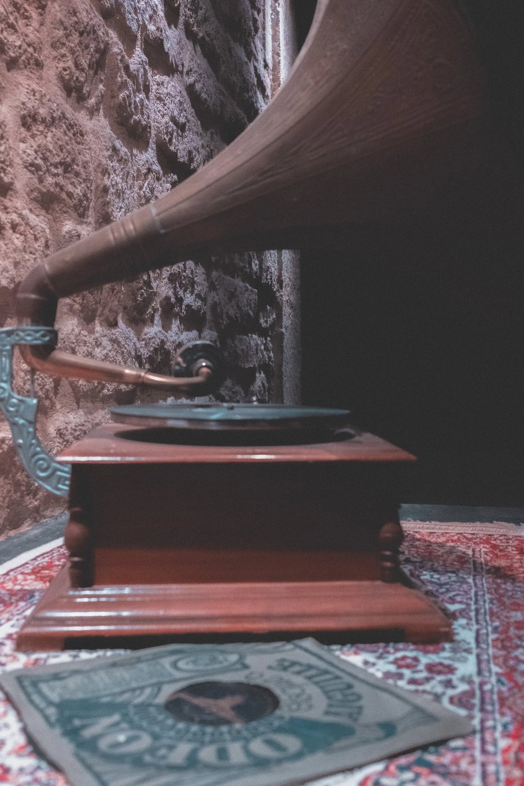 A vintage gramophone with a wooden base and a large horn, positioned next to a decorative rug and a vinyl record.