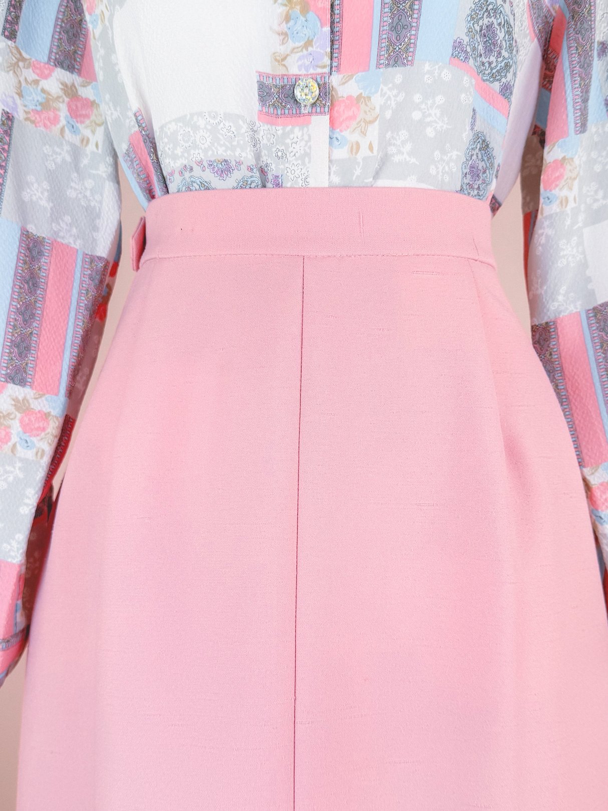 Blush pink skirt suit with a patterned blouse featuring floral and geometric designs, typical of 1970s fashion.