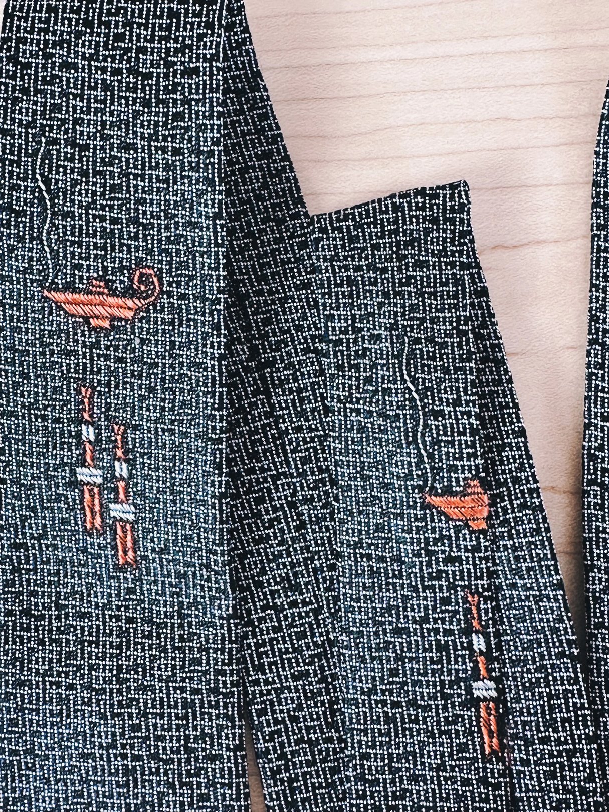 Close-up of a patterned fabric featuring embroidered designs in orange and white on a textured dark background.