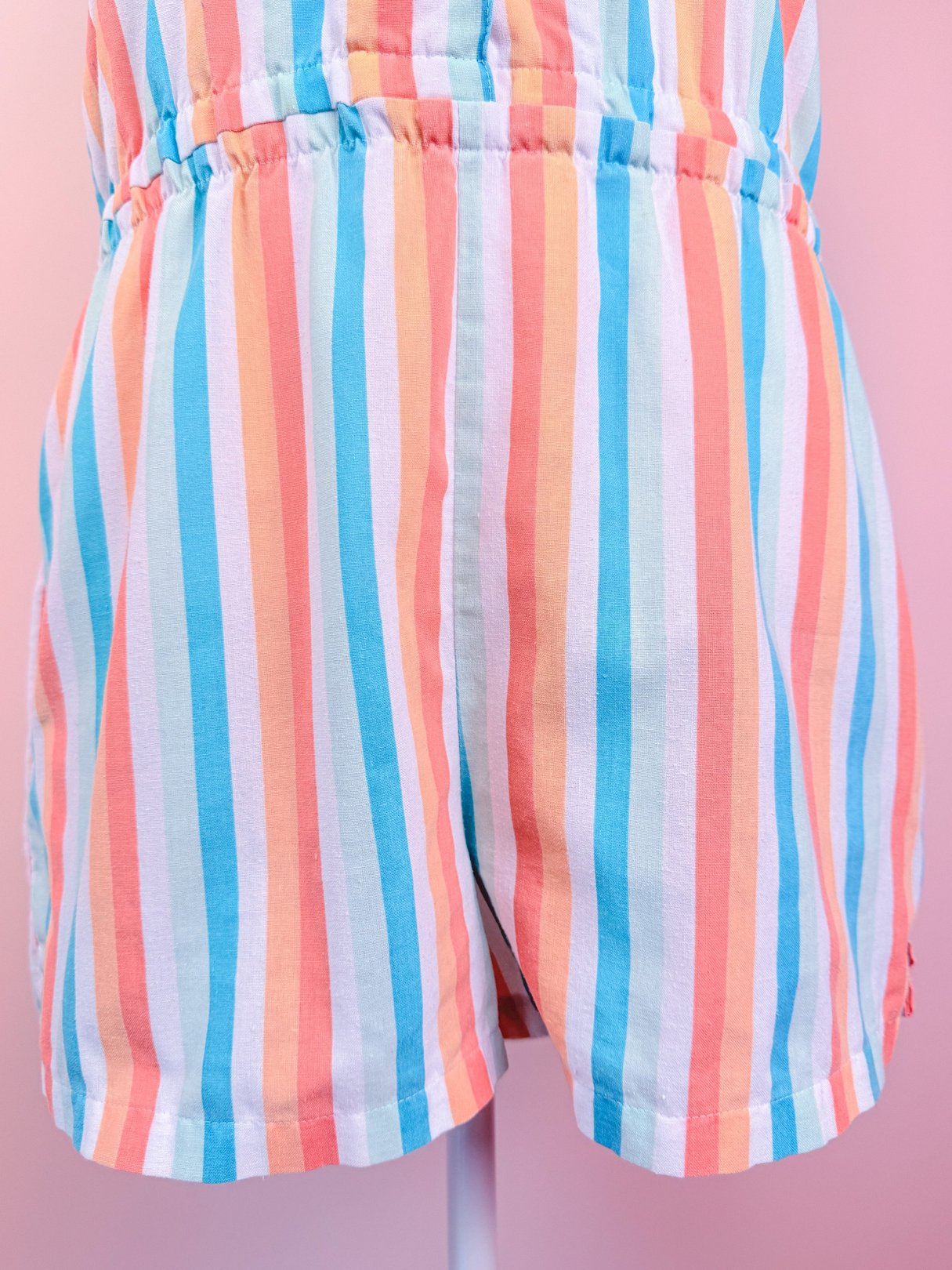 Blue and multicolored striped romper for women with a waist elastic and short shorts, inspired by 1980s fashion.