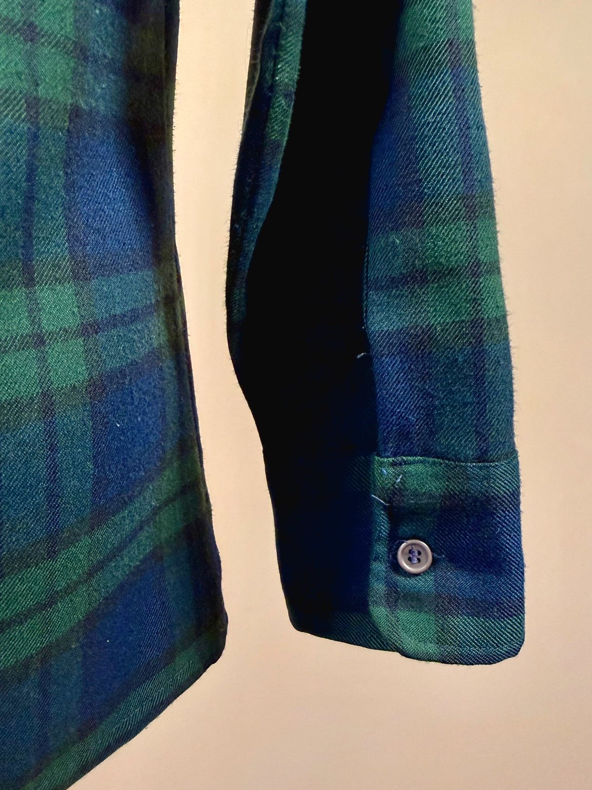 Navy blue and green plaid fabric with visible shirt cuff featuring a single button typical of men's fashion from the 1950s.