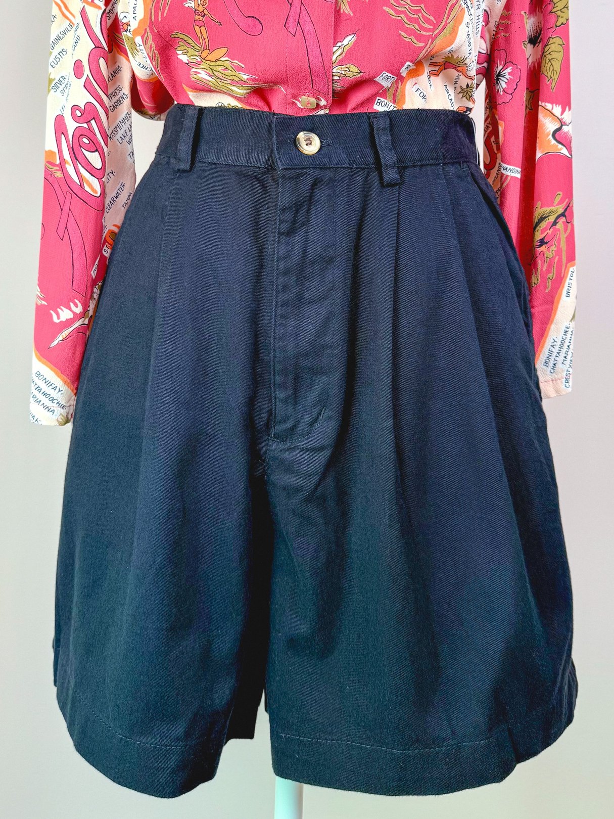 High-waisted black women's shorts with pleats, styled in a 1980s fashion.