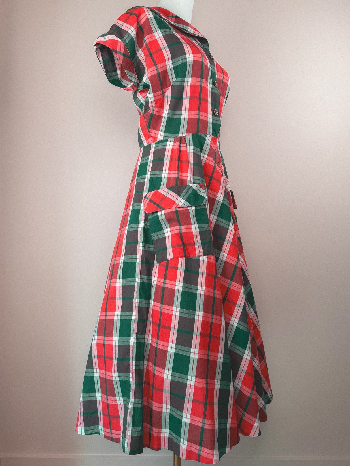Red and green plaid dress with a collared neckline, short sleeves, and side pockets, inspired by 1950s fashion for women.
