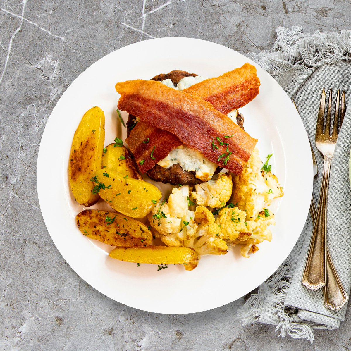 A juicy Cajun-seasoned beef burger topped with creamy melted bleu cheese and savory uncured chicken bacon served alongside golden roasted fingerling potatoes and tender cauliflower florets.