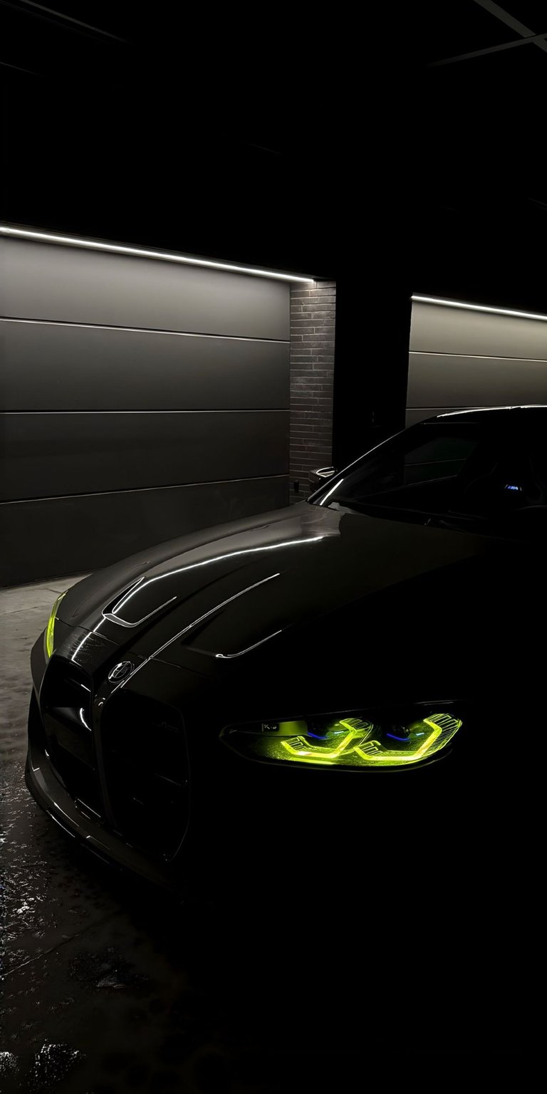 This high-contrast BMW M4 G82 4K wallpaper features the iconic yellow daytime running lights against a deep black backdrop. Optimized for iPhone, this OLED / AMOLED wallpaper highlights the aggressive hood lines and signature kidney grille in a moody, cinematic garage setting.