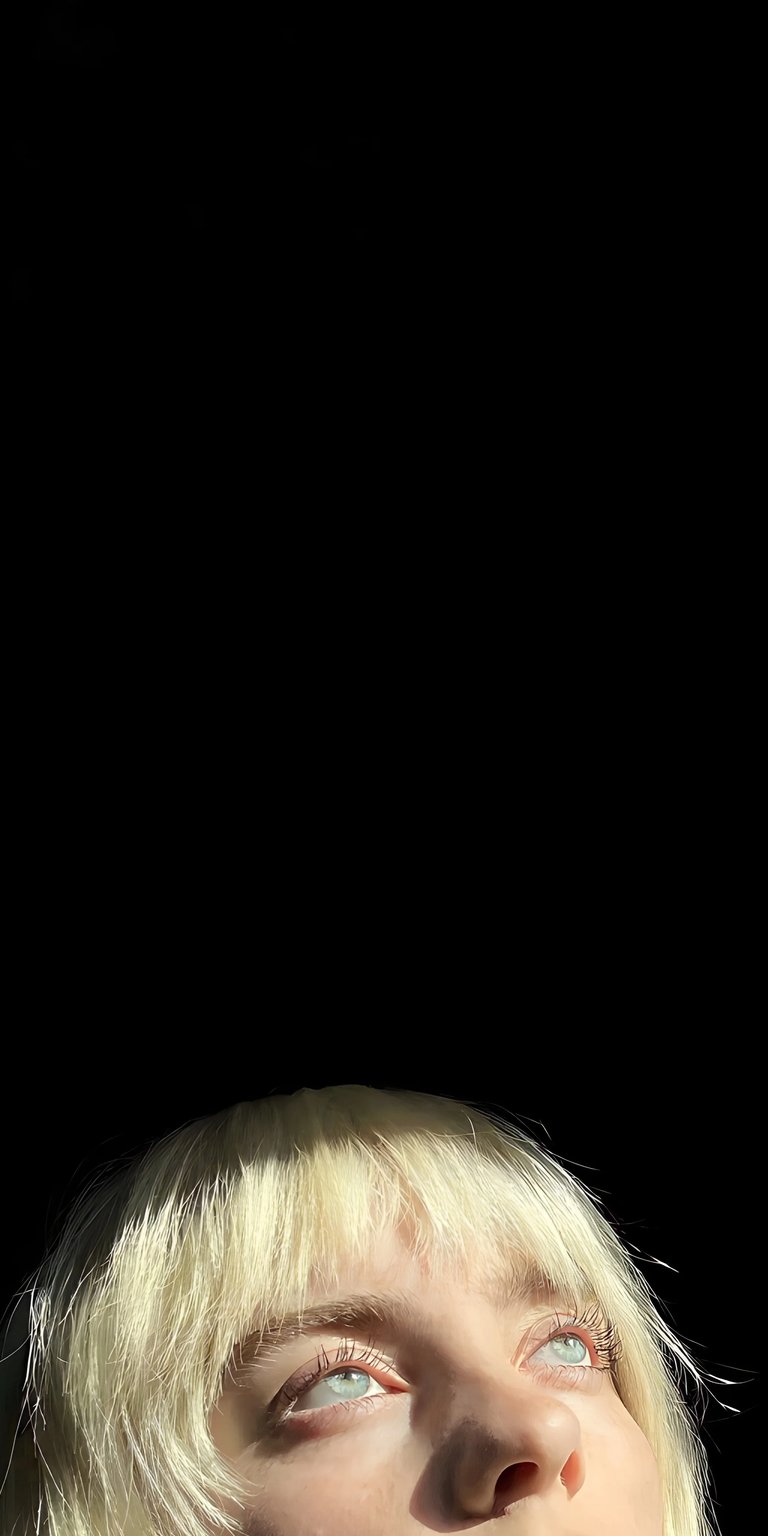 Download this stunning Billie Eilish 4K wallpaper for your iPhone, featuring a close up of her face. The wallpaper captures her platinum blonde hair, striking blue eyes, and upward gaze.