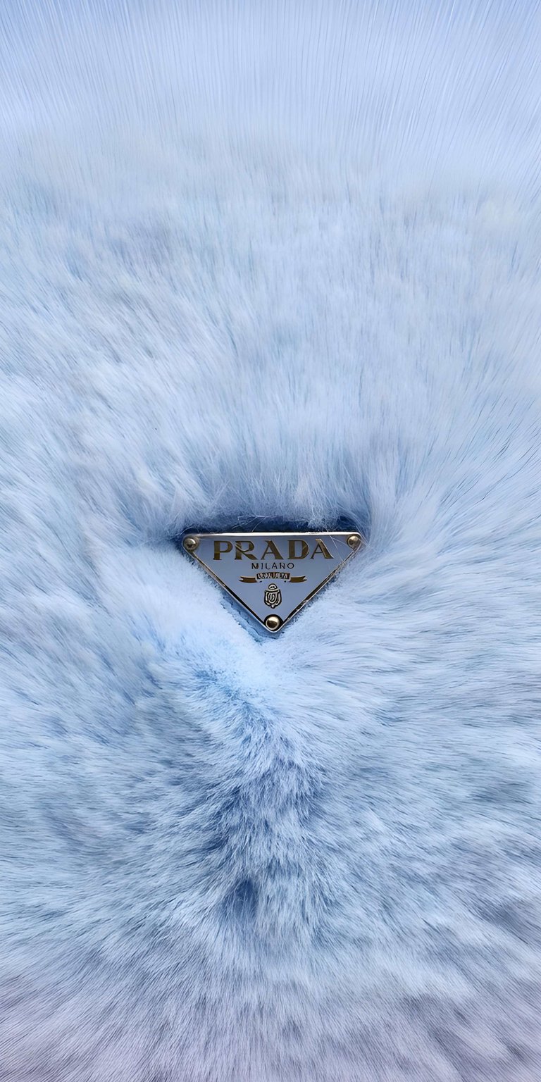 Elevate your screen with the ultimate high-fashion aesthetic. This wallpaper features the prestigious Prada Milano triangle logo nestled deep within a soft, plush, light blue faux fur texture. The icy blue tones and the tactile feel of the fabric provide a sophisticated, cozy, and luxurious vibe that fits perfectly with minimal or "clean girl" aesthetic setups.