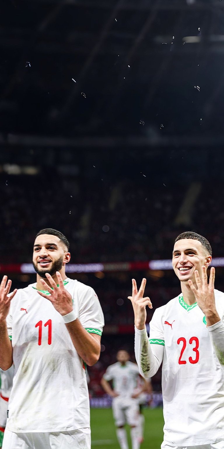 Celebrate the brotherhood of Moroccan football with this 4K wallpaper featuring stars Achraf Hakimi and Hakim Ziyech in their national team kits. This iPhone wallpaper showcases the duo sharing a moment of victory against a blurred stadium backdrop, making it a must-have for Atlas Lions fans.