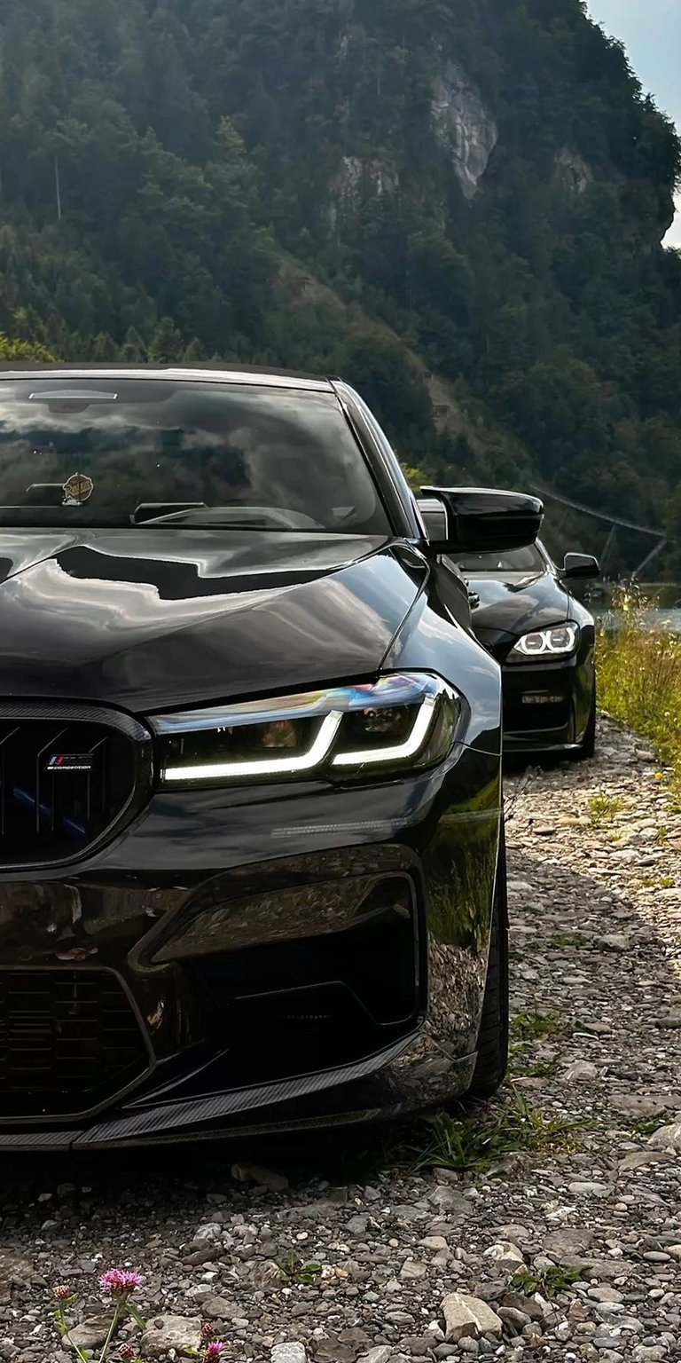This stunning BMW M5 4K wallpaper is perfect for your iPhone, showcasing the sleek headlights and aggressive front grill. Enjoy the view of two black BMWs parked on a rocky road.