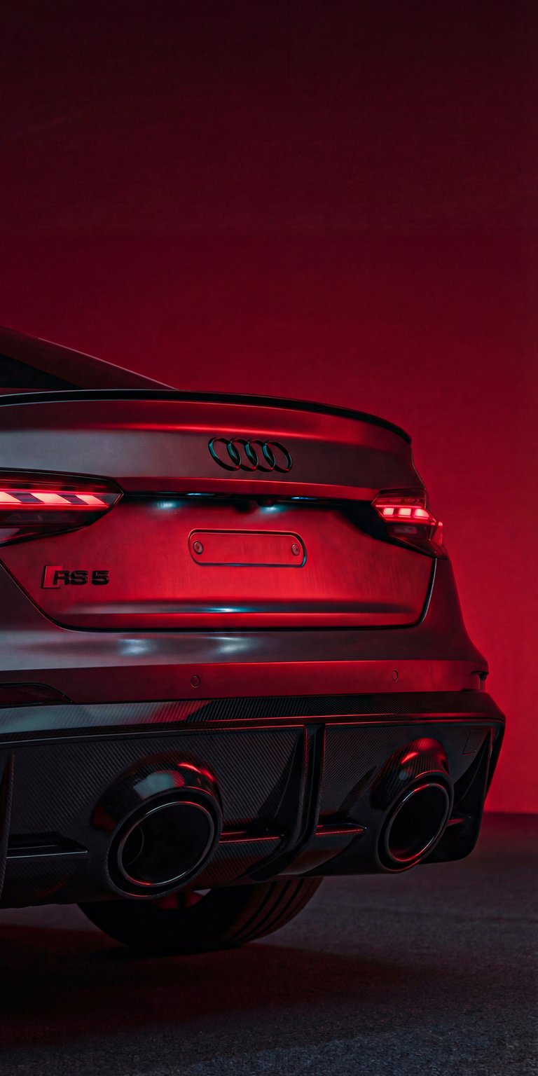 This detailed 4K wallpaper focuses on the glowing red LED tail lights and rear diffuser of an Audi. The dark shadows make it an ideal OLED wallpaper for a clean iPhone look.