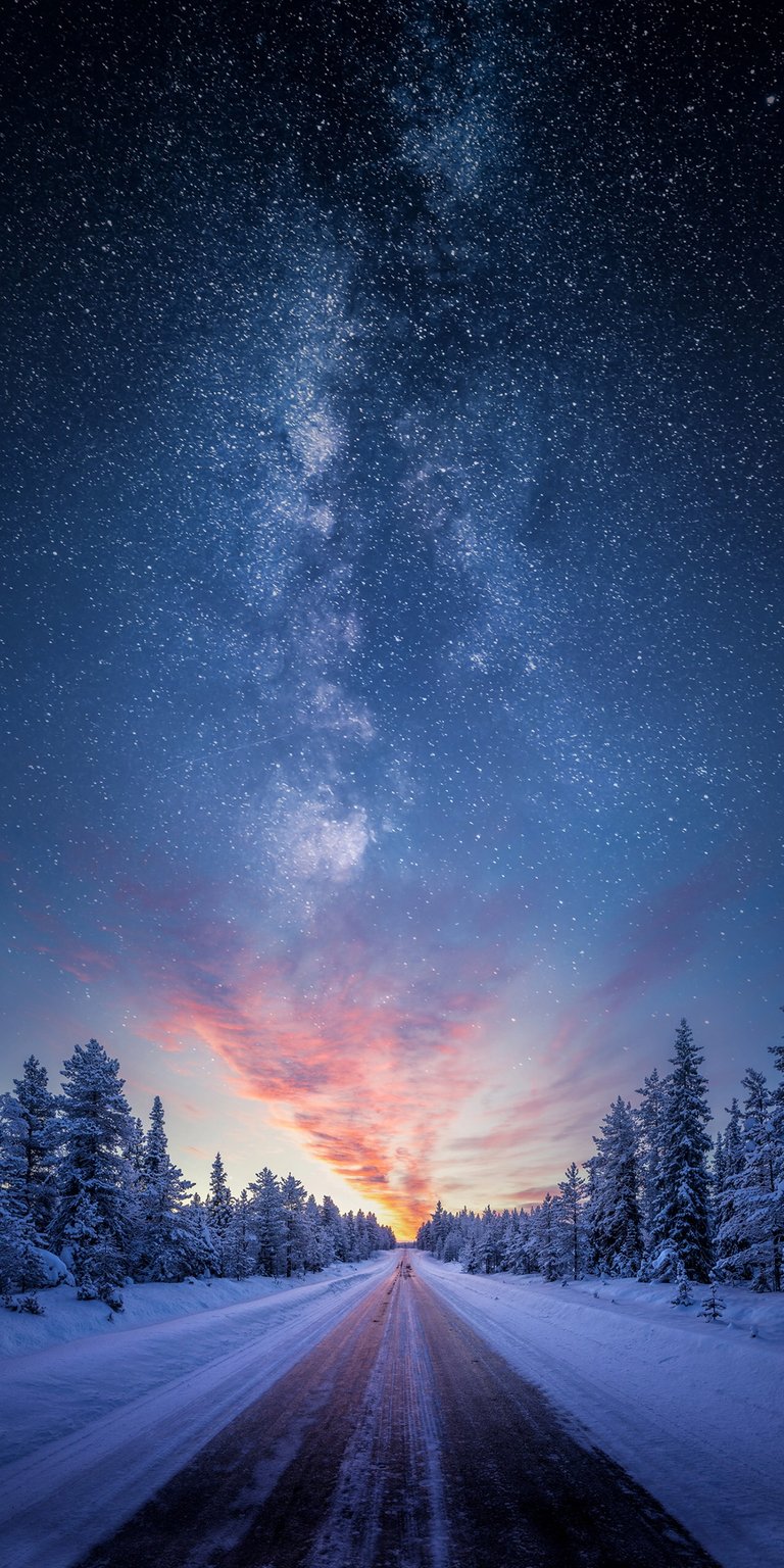 Download this stunning Milky Way 4K wallpaper for your iPhone, showcasing a road leading towards a vibrant pink horizon, framed by snow-laden pine trees. This beautiful wallpaper captures the serene beauty of the night sky.