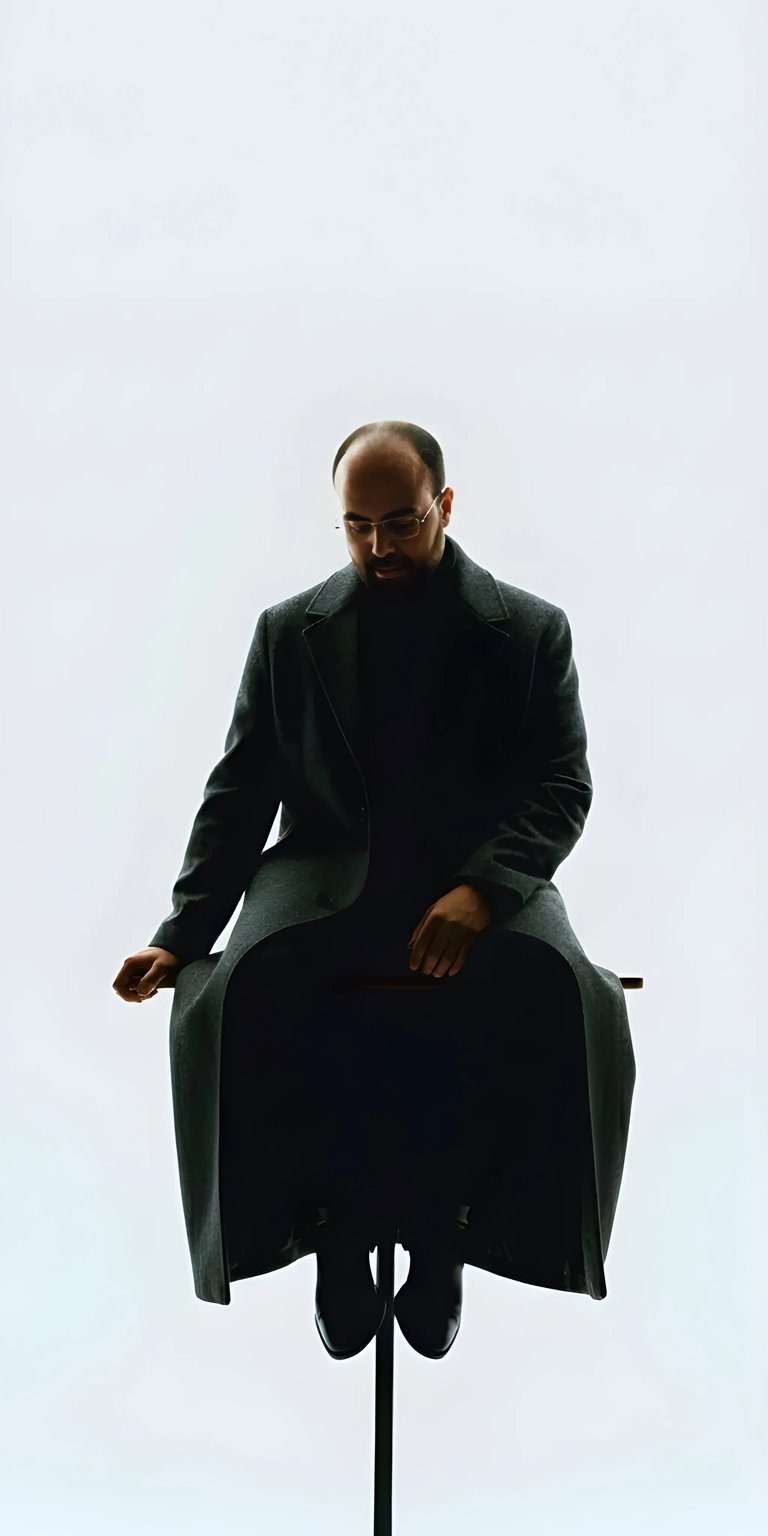 This high-contrast OLED / AMOLED wallpaper features Danny Slicer in a long trench coat positioned against a bright, minimalist background. A sharp 4K wallpaper for iPhone, it highlights clean lines and a modern, cinematic silhouette.