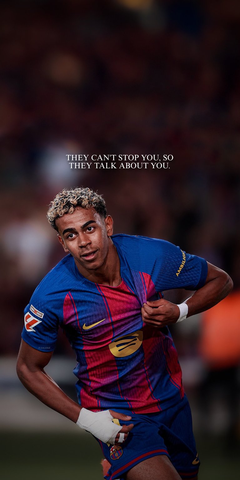 Get this Lamine Yamal wearing a blue and red striped FC Barcelona jersey and is on a soccer field wallpaper in high-quality HD 4K. With "THEY CAN'T STOP YOU SO THEY TALK ABOUT YOU" quote at the top.