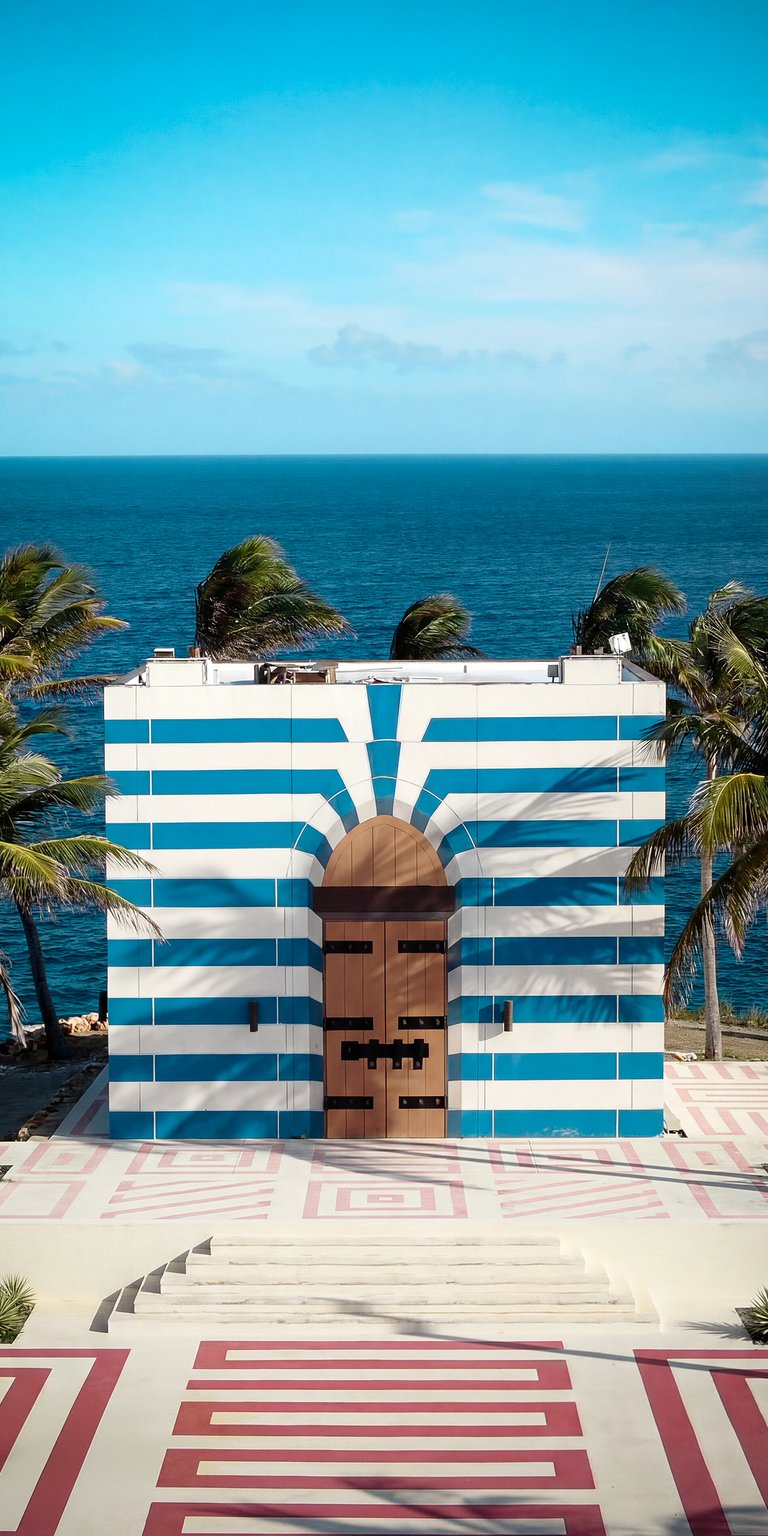 This aesthetic wallpaper features a vibrant blue and white striped building overlooking a deep blue ocean. Perfect for your iPhone, this wallpaper captures a sunny, coastal mood with palm trees and geometric red patterns on the ground.