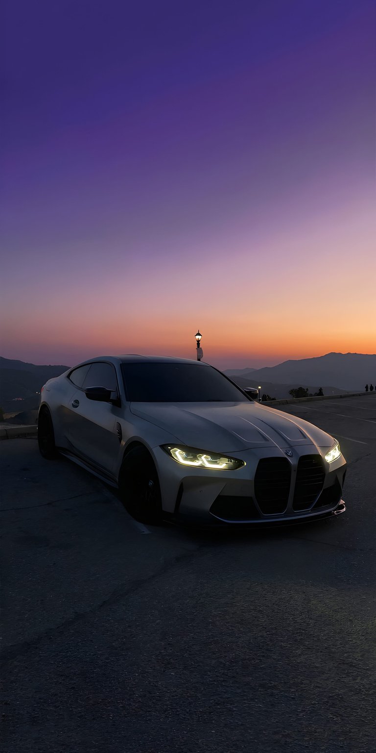 This high-resolution 4K wallpaper features a sleek silver BMW M4 parked against a stunning purple and orange sunset. Perfect for an iPhone lock screen, this aesthetic wallpaper captures the cinematic lighting and sharp contours of the vehicle in a serene mountain setting.