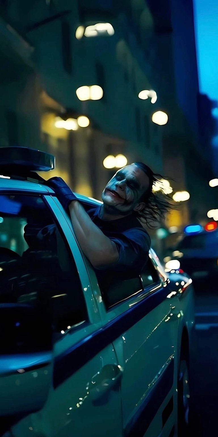 Download this striking Joker 4K wallpaper for your iPhone, showcasing him leaning out of a light blue car. The image features a blurred cityscape backdrop and blue police lights.