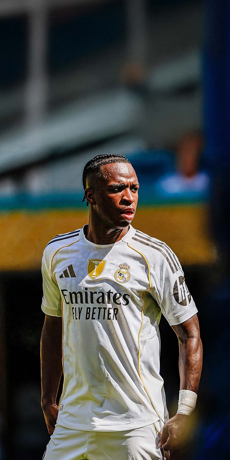 Download this amazing Vinicius Junior 4K wallpaper for your iPhone, showcasing him in his Real Madrid kit. This wallpaper captures the star forward with braided hair, wearing a white uniform with the Emirates logo.
