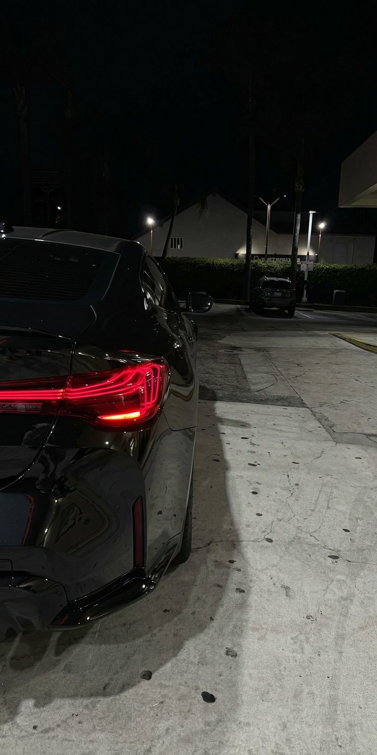 Get this sleek BMW wallpaper for your iPhone, showcasing its distinctive red tail light and glossy black paint in stunning 4K resolution. The subtle lighting and concrete surface highlight the car's modern design, making this wallpaper a must-have.