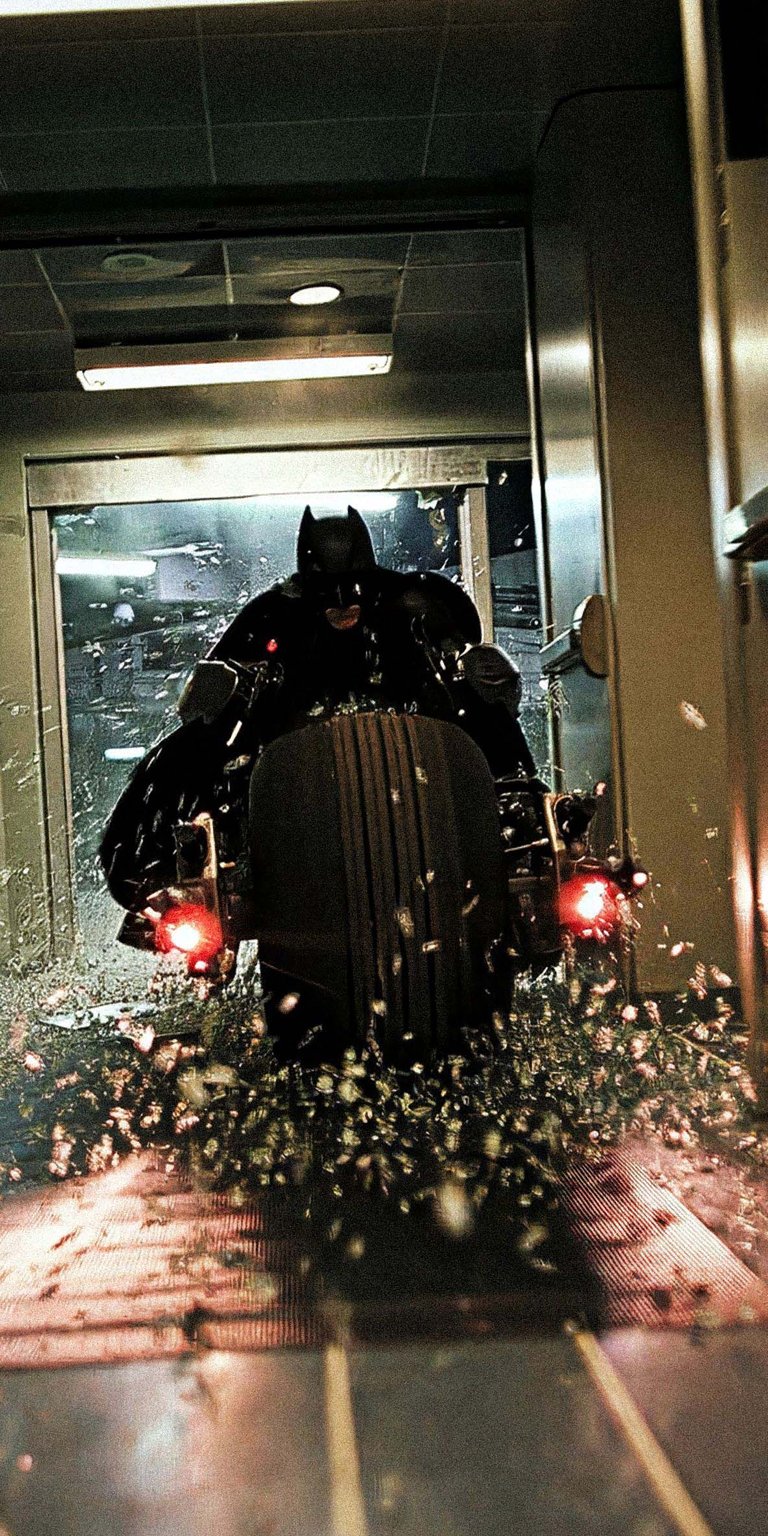 Download this Batman wallpaper in stunning 4K for your iPhone, showcasing Batman on his Batcycle. Notice the red taillights, the splattering water, and the industrial setting.