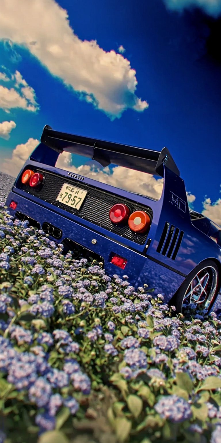 Download this cool Ferrari F40 wallpaper in 4K for your iPhone. This wallpaper features a blue Ferrari F40 parked in a field of purple flowers with its iconic rear wing and quad exhaust pipes visible.