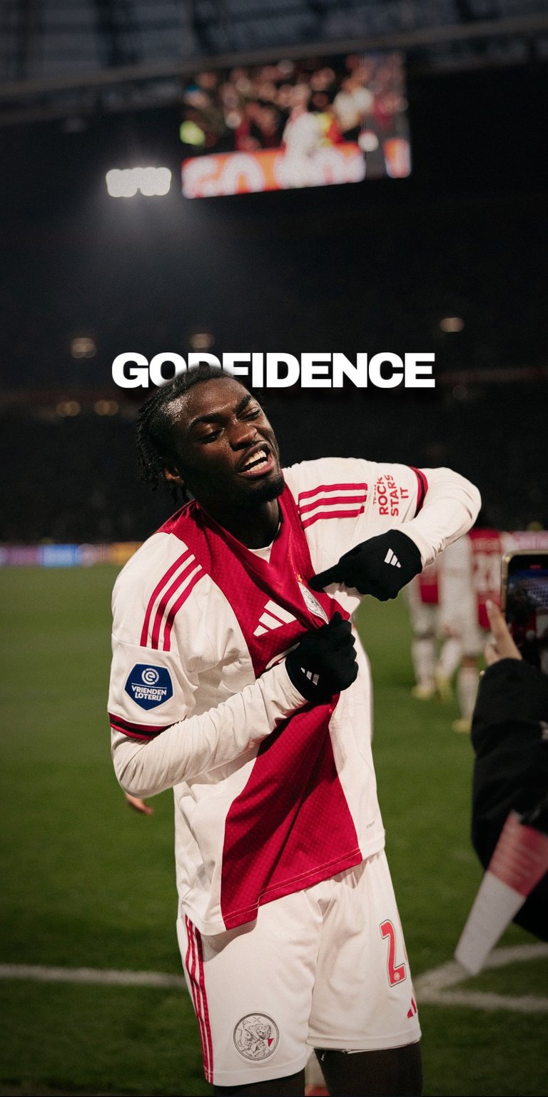 Showcase the raw power and confidence of Ajax’s young prospect, Jorthy Mokio. This wallpaper features a high-energy celebration shot with the unique "GODFIDENCE" typography. With the classic red and white Ajax kit popping against a dark stadium background, it’s the perfect high-res screen for fans of the Eredivisie giants.