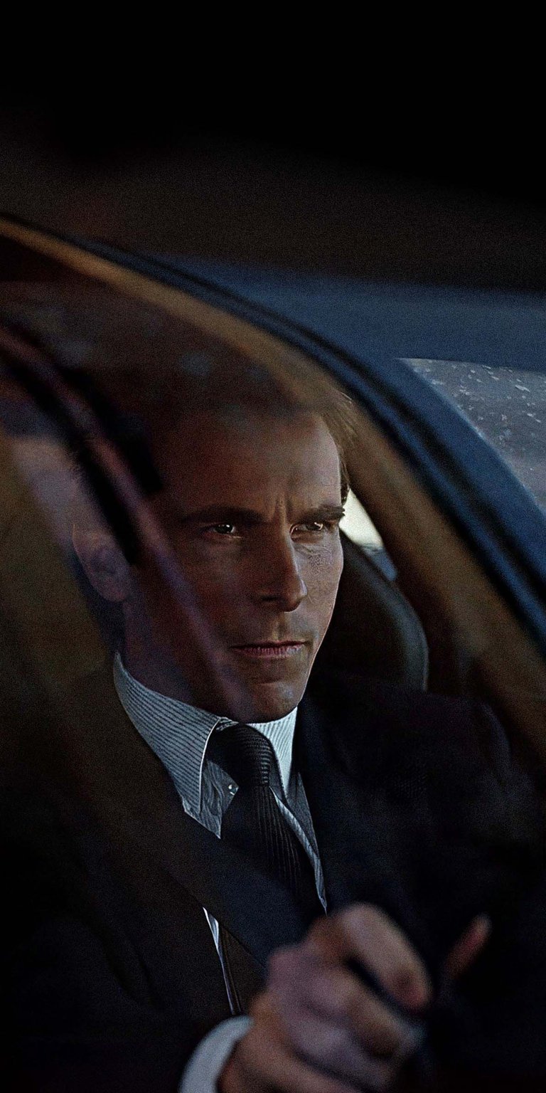 Download this Patrick Bateman 4K wallpaper for your iPhone to showcase a sophisticated look. Notice his striped dress shirt, dark suit, and the raindrops on the car window in this striking wallpaper.