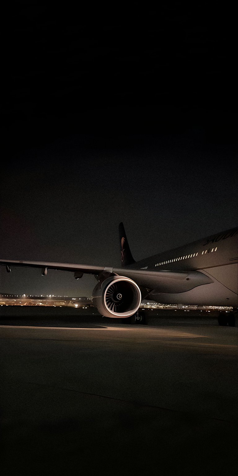 This 4K wallpaper features a high-contrast view of a jet engine and wing at night, perfect for fans of aviation and OLED / AMOLED wallpapers. The deep blacks and warm ground lighting create a sophisticated look for your iPhone lock screen.