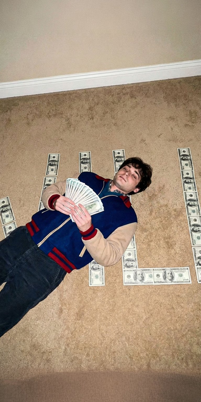 This nostalgic live wallpaper features the character Will Byers from Stranger Things. Will is lying on the floor, surrounded by dollar bills arranged into a pattern (not fully forming a word, but scattered), and is holding a large fan of money. He is dressed in his signature 80s style jacket (blue and red). This image blends the show's iconic characters with a unique, money-themed aesthetic.