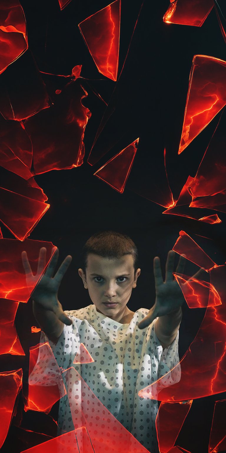 Get this Eleven 4K wallpaper for your iPhone; it features sharp, fiery shards surrounding her. She wears a patterned gown and gazes intently with both hands up.