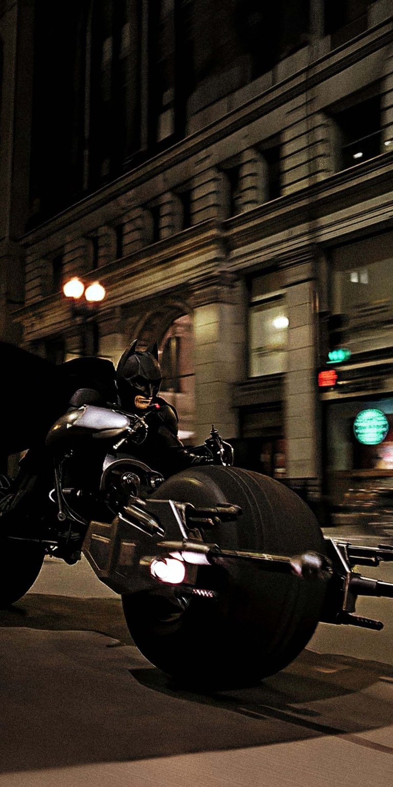 Get this thrilling Batman wallpaper in stunning 4K, capturing the dark knight on his Batpod racing through the city streets, illuminated by vintage streetlights. This iPhone wallpaper showcases the intense action and iconic design of the Batpod.