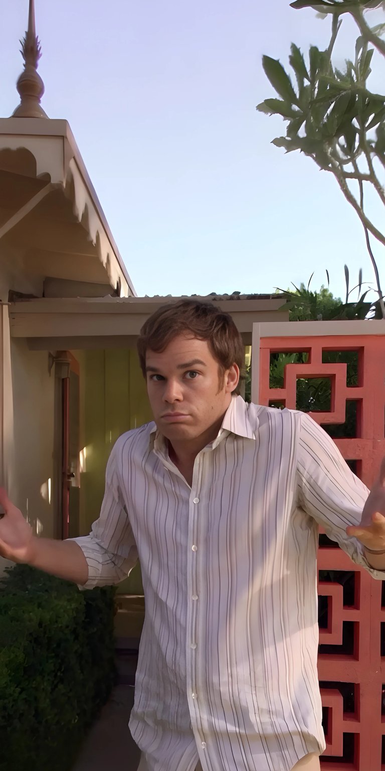 Download this Dexter Morgan 4K wallpaper for your iPhone. The wallpaper features Dexter in a striped shirt with an expression of confusion, standing next to an intricate, coral-colored wall.