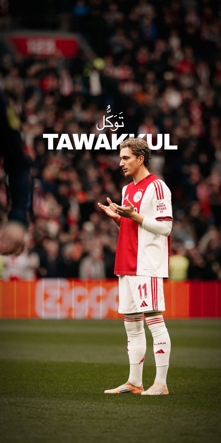 A powerful sports wallpaper featuring Dušan Tadić in his Ajax kit, captured in a moment of spiritual reflection. The image features the Arabic word "Tawakkul" (Trust in God) in elegant calligraphy, blending professional football with deep personal faith. Perfect for fans of the Eredivisie and those looking for inspirational Islamic sports backgrounds.