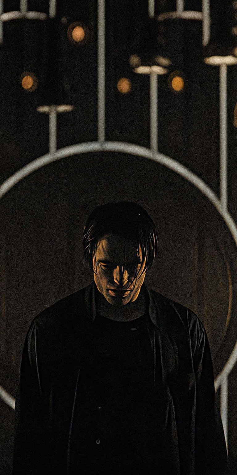 Download this Robert Pattinson 4K wallpaper for your iPhone, showcasing him in a dimly lit setting with a circular backdrop. This wallpaper highlights his sleek, dark hair and the dark jacket he is wearing.